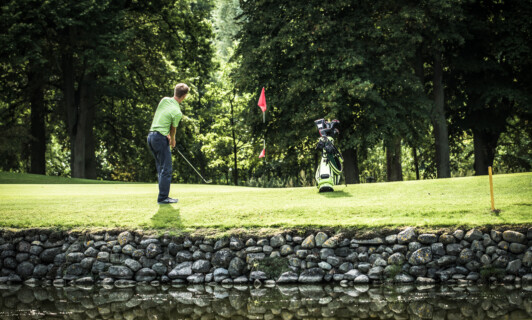 Ein Golfer auf der SCHLOSS Golfanlage mit Teich.