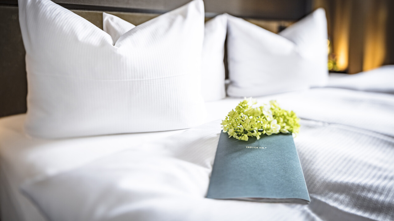 Das Bett in der Schlosssuite im Schloss Fleesensee mit einem Flyer und Blumen.