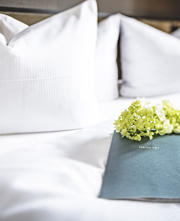 Das Bett in der Schlosssuite im Schloss Fleesensee mit einem Flyer und Blumen.