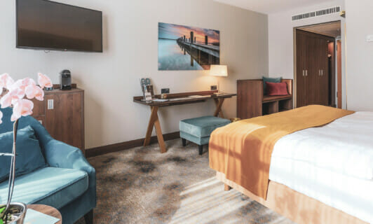 Das Deluxe Zimmer mit Fernseher, Sesseln, kleinem Schreibtisch und Bett im Schlosshotel Fleesensee.