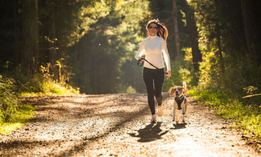 Eine Frau geht mit ihrem Hund im Wald joggen.