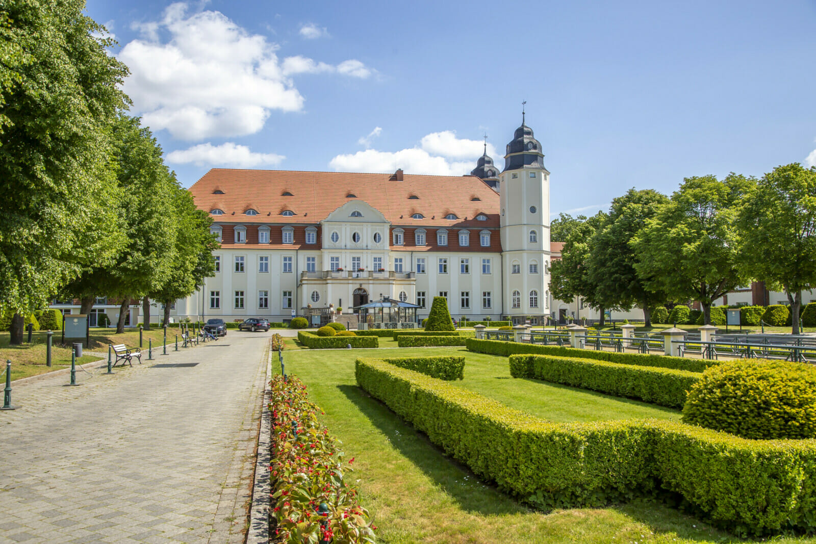 Die Auffahrt des Schloss Fleesensee mit Zierhecken und gesäumt von Bäumen.