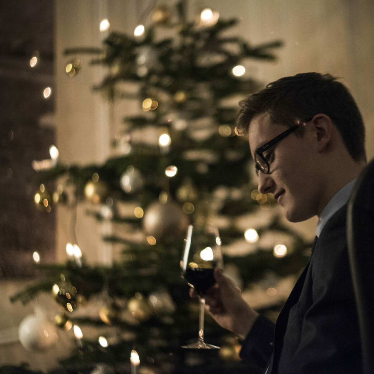 Ein Mann sitzt vor einem Weihnachtsbaum und trinkt Wein.