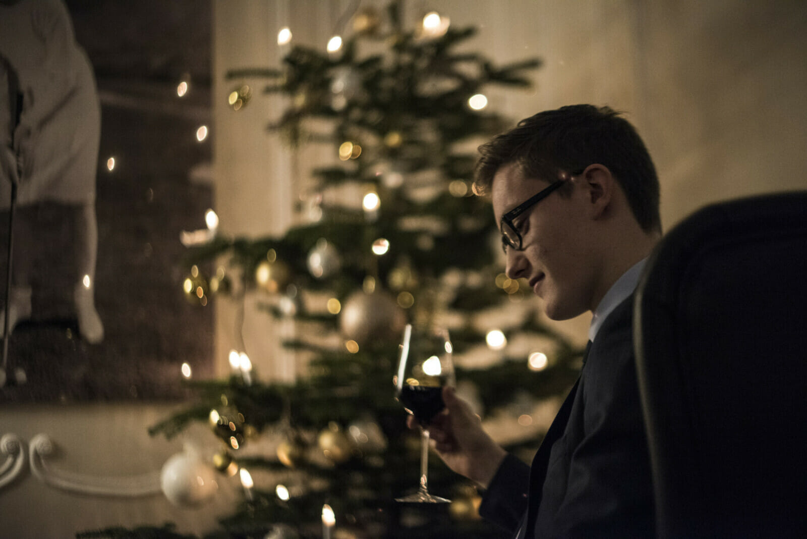 Ein Mann sitzt vor einem Weihnachtsbaum und trinkt Wein.