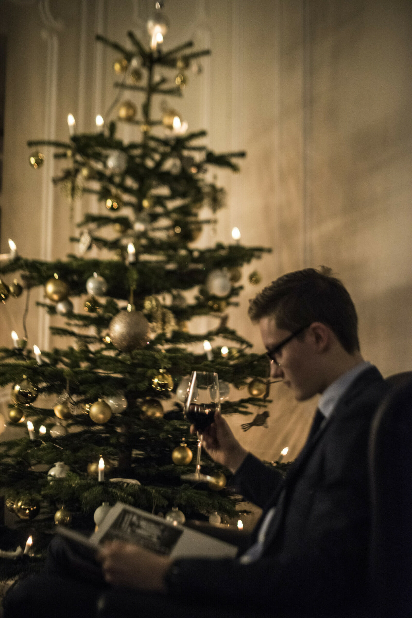 Ein Mann sitzt vor einem Weihnachtsbaum und trinkt Wein.