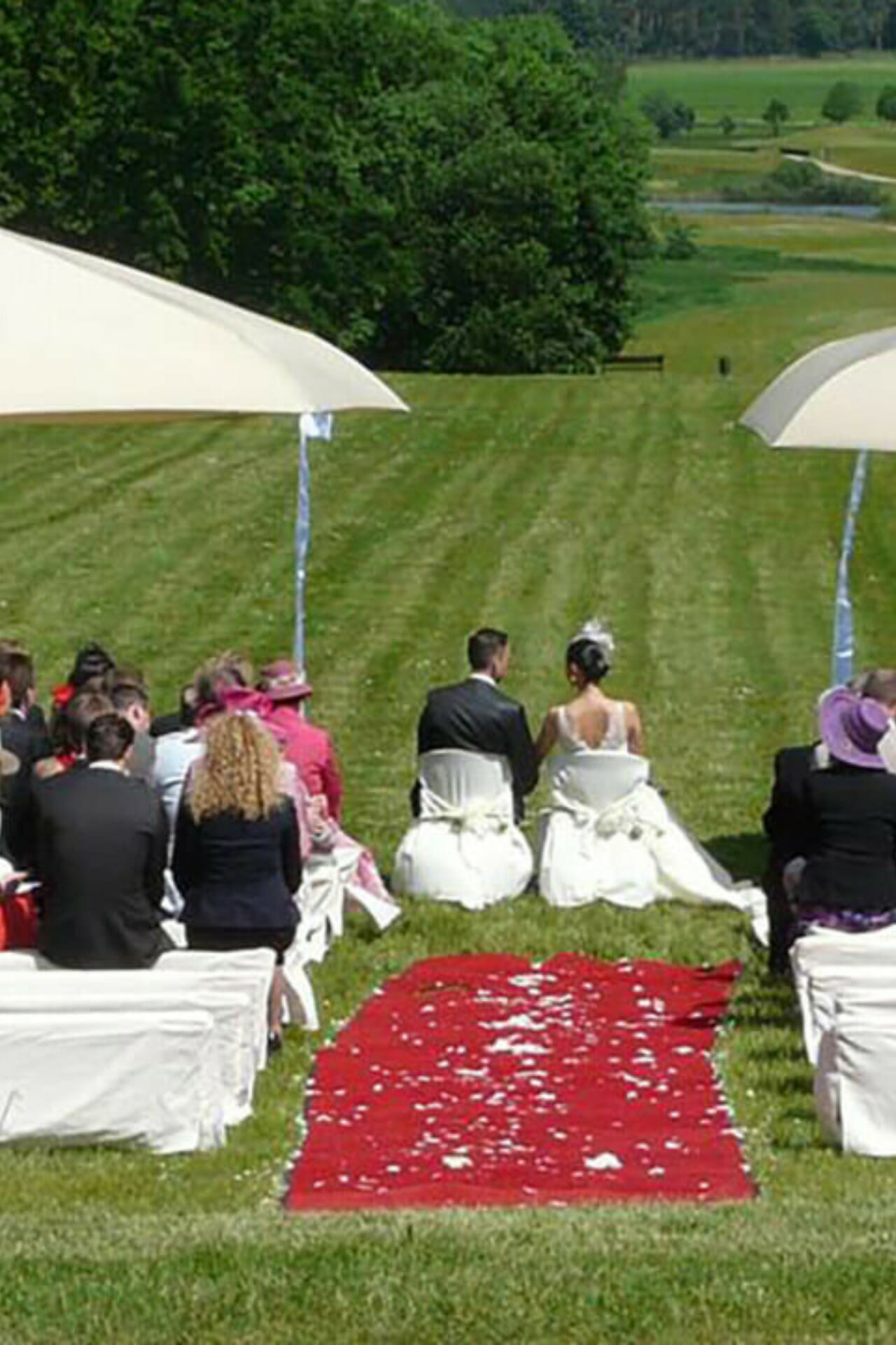 Ein Brautpaar sitzt auf Stühlen auf einer Wiese hinter dem Schloss Fleesensee.