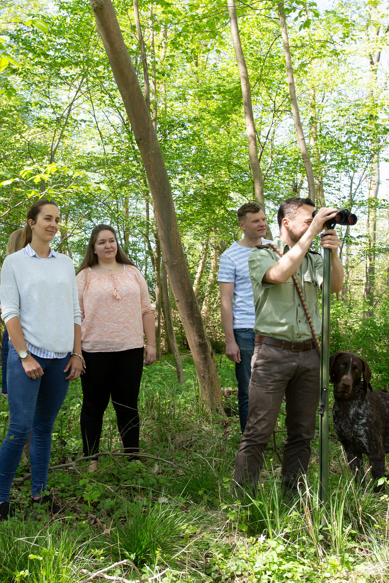 Eine Gruppe im Wald auf der Pirsch mit einem Jäger und dessen Hund.