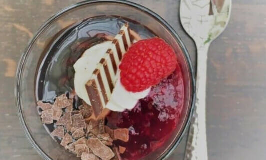 Ein Dessert im Glas mit Himbeere und Löffel.