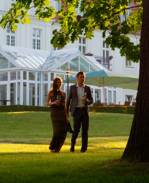 Ein Paar geht mit Wein im Schlosspark spazieren.